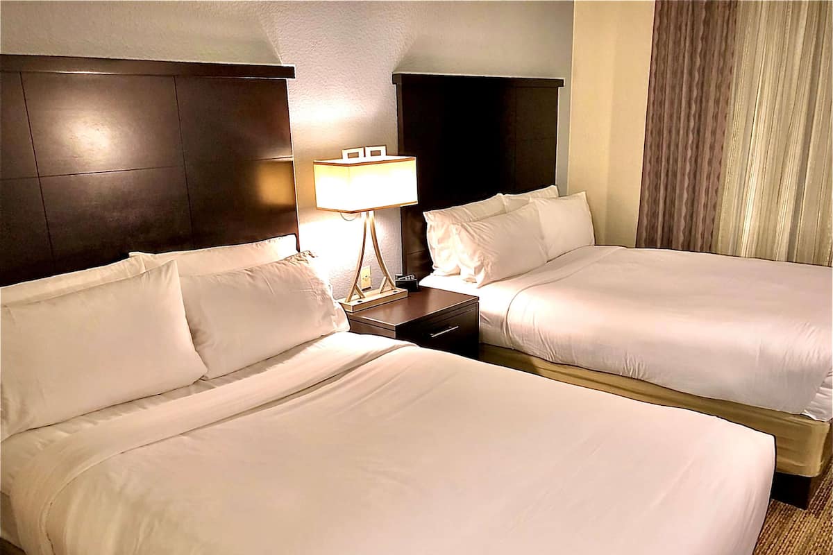 Ein Hotelzimmer mit zwei Betten, einem Nachttisch mit Lampe und einem dunklen Kopfteil.