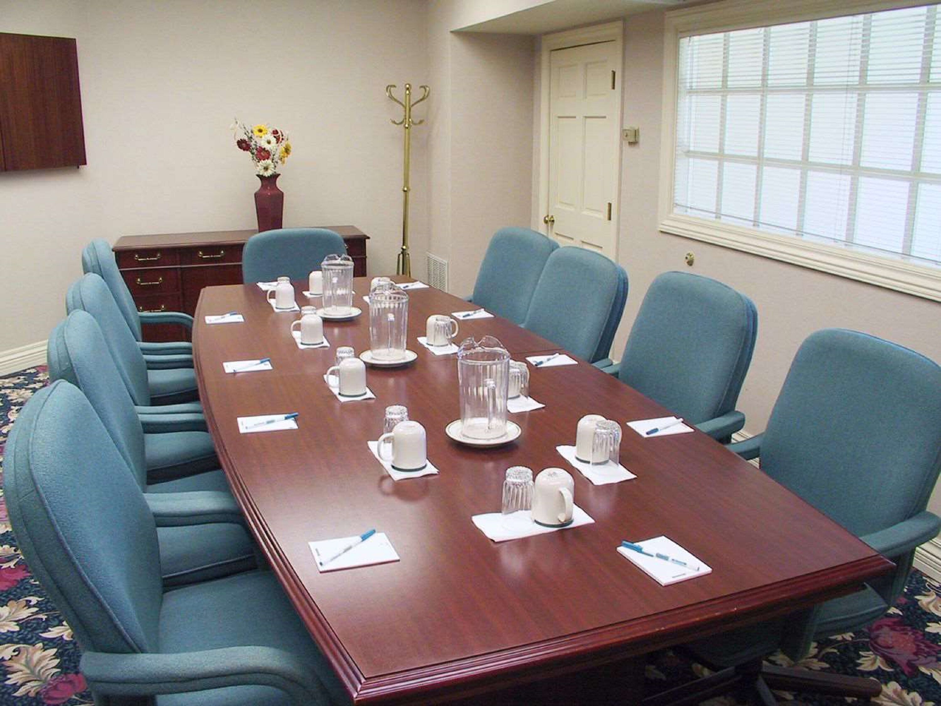 A conference room with a long table, blue chairs, and various items like cups and a vase of flowers.