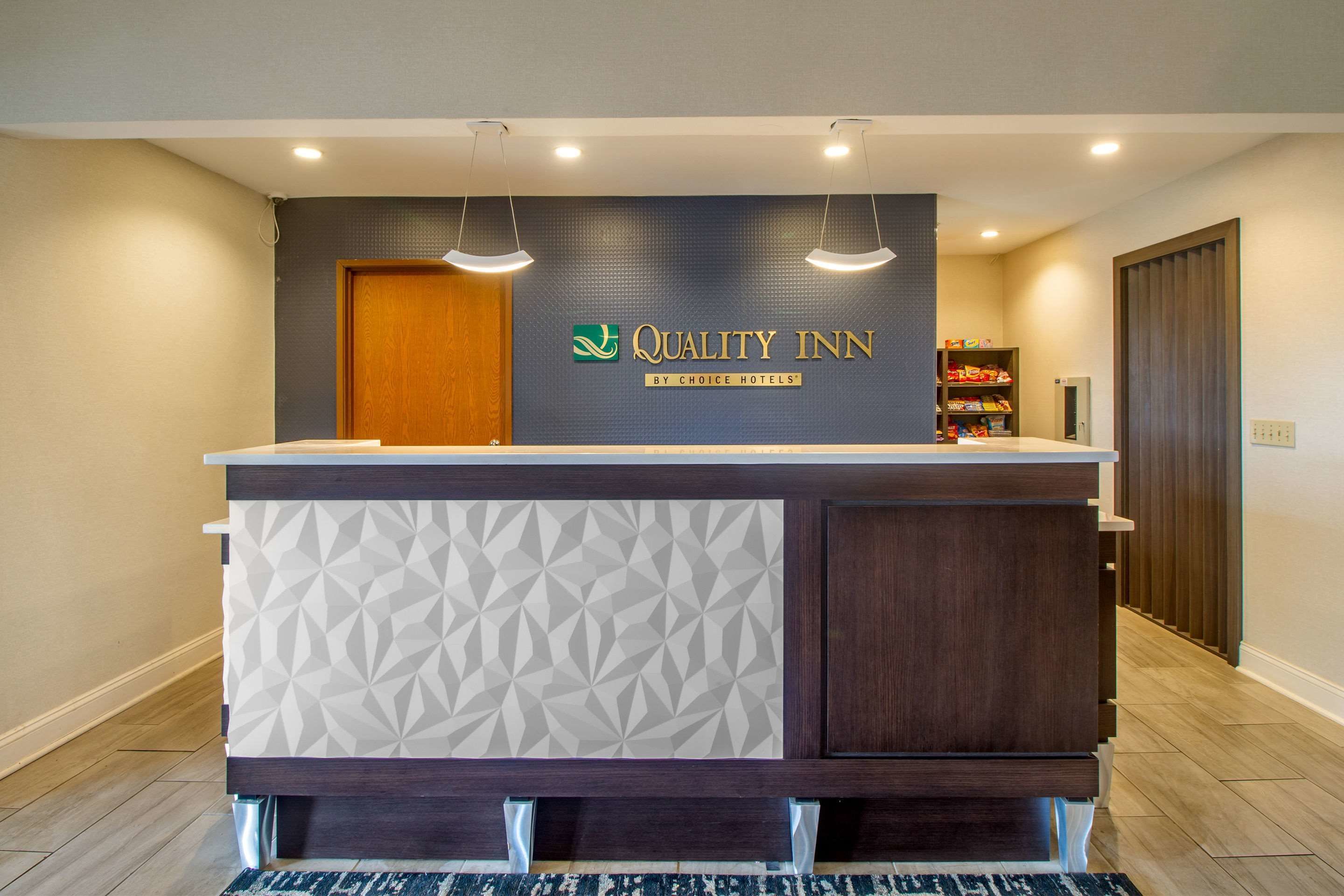 A reception desk with a geometric pattern, a sign for Quality Inn by Choice Hotels, and a wooden door in the background.