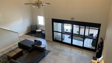 Um hall espaçoso com design moderno, com uma ampla área de estar com sofá e poltronas, um ventilador de teto e vista para a área externa através de grandes janelas.