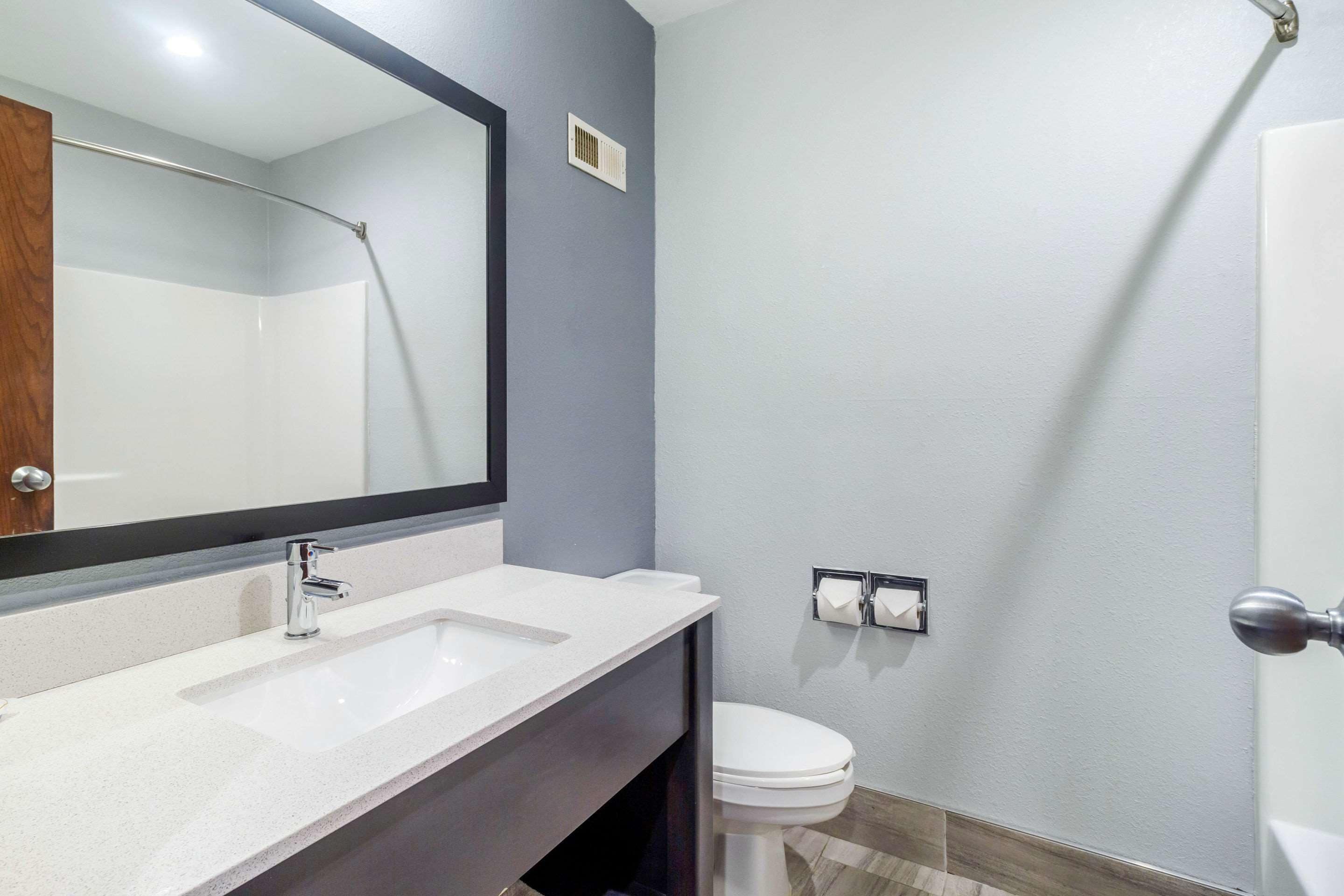 A modern bathroom with a large mirror, two sinks, a toilet, and a shower.