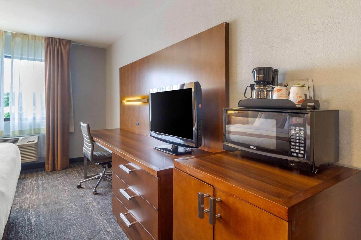 Una habitación de hotel con escritorio de madera, televisor de pantalla plana, microondas y cafetera.