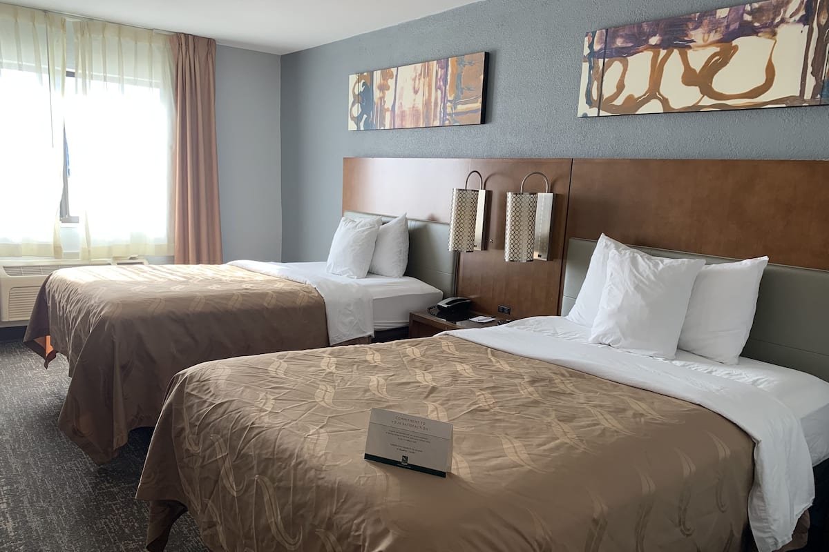 A hotel room with two beds, a nightstand, a telephone, and artwork on the walls.
