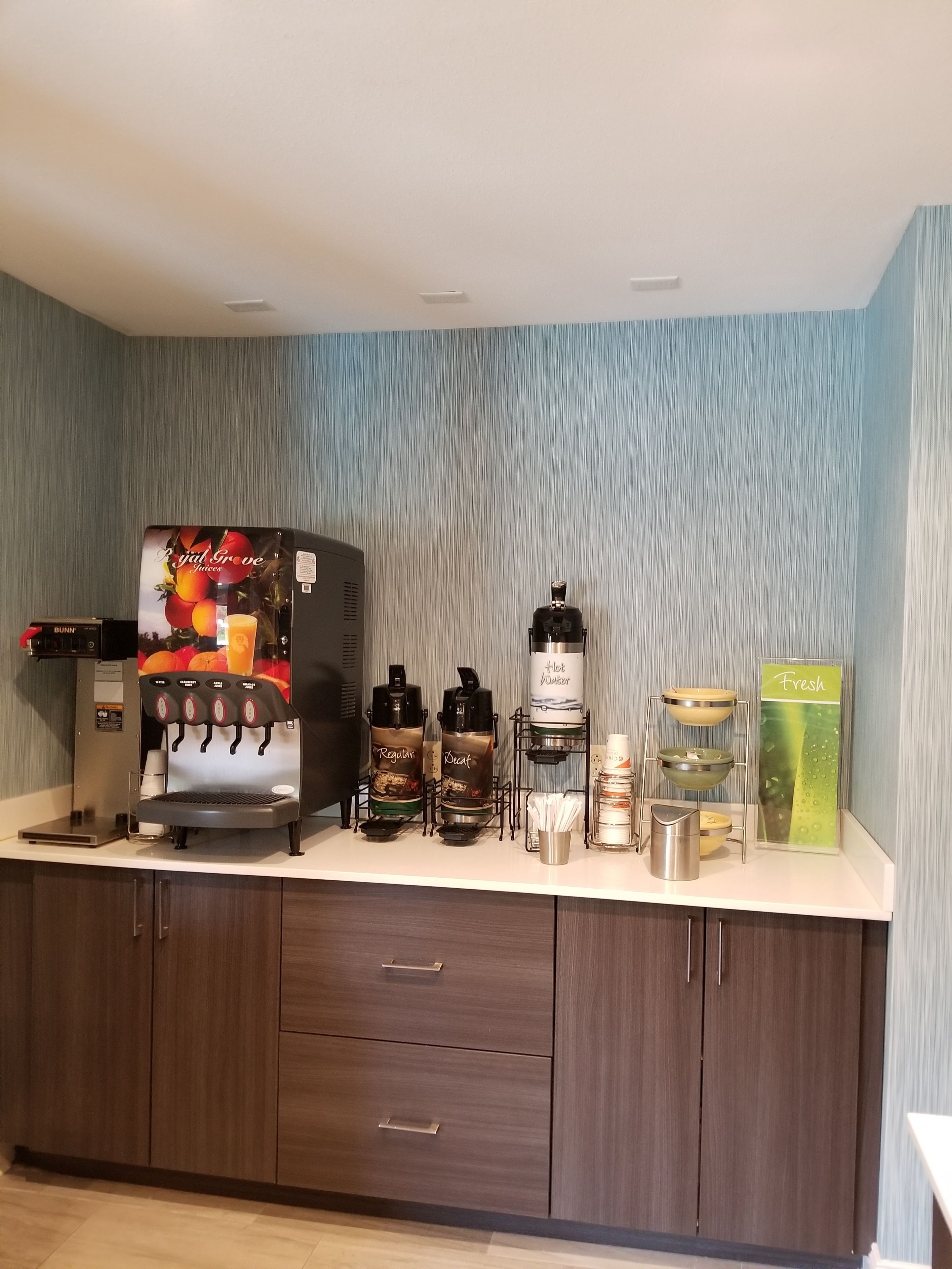 A coffee station with a branded coffee machine, multiple dispensers, and a fresh juice dispenser.