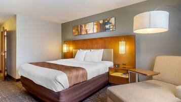 Quarto de hotel com uma cama grande, mesas de cabeceira, uma cadeira e uma obra de arte na parede.
