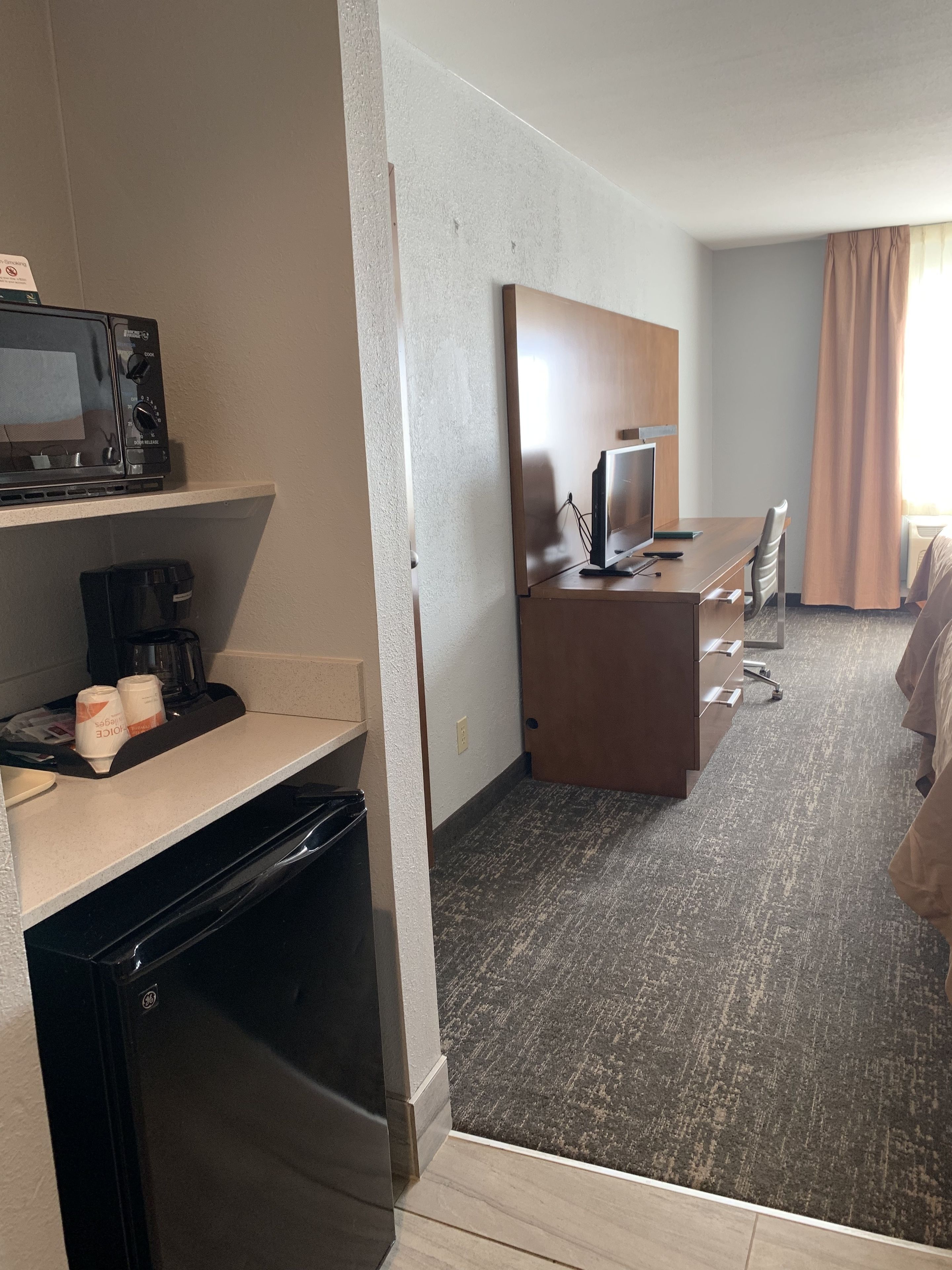 A hotel room with a kitchenette, a bed, a desk with a computer, and a TV.