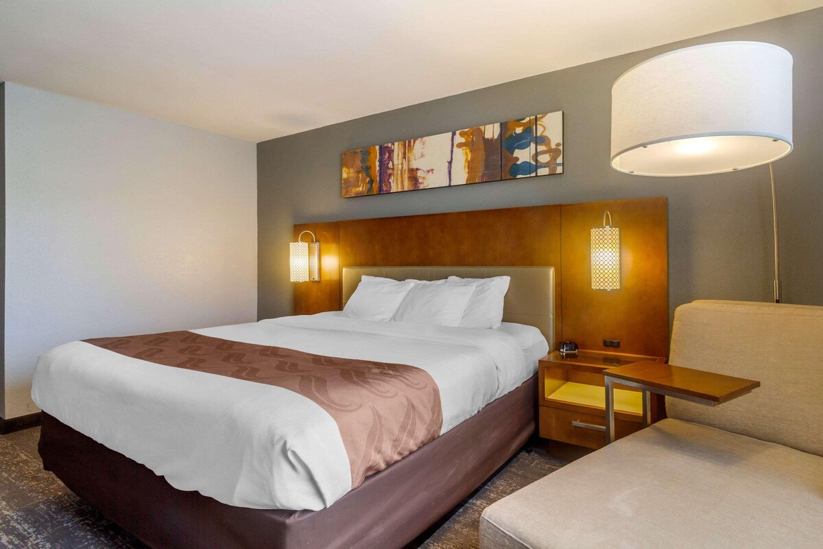 A hotel room with a large bed, bedside tables, a chair, and a painting on the wall.
