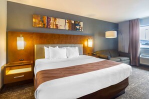 A hotel room with a large bed, a headboard, two bedside tables with lamps, a sofa, and a painting on the wall.
