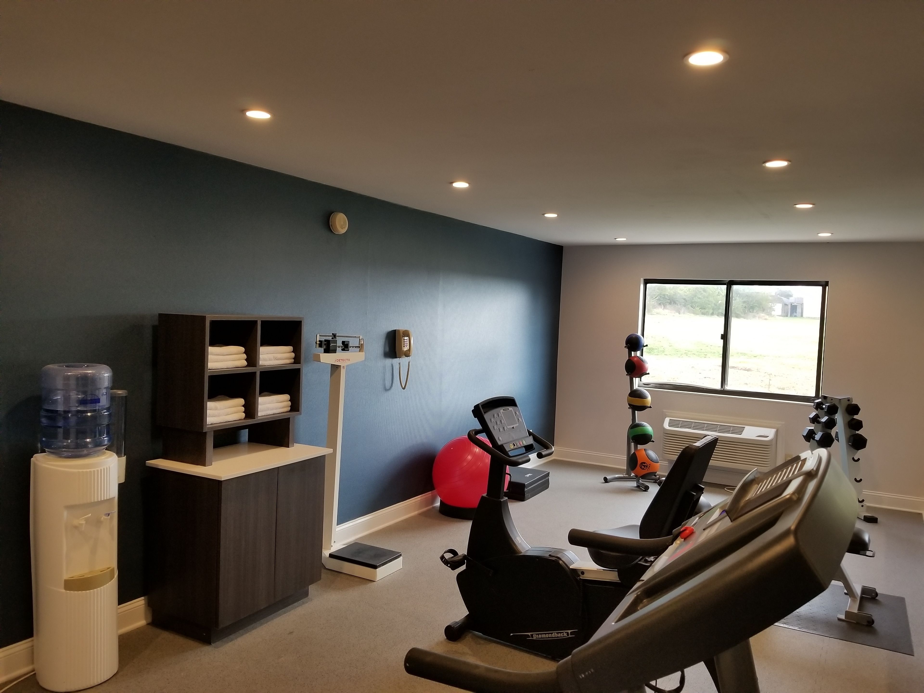 Un gimnasio con equipo de ejercicio, dispensador de agua, teléfono y ventana con vistas.