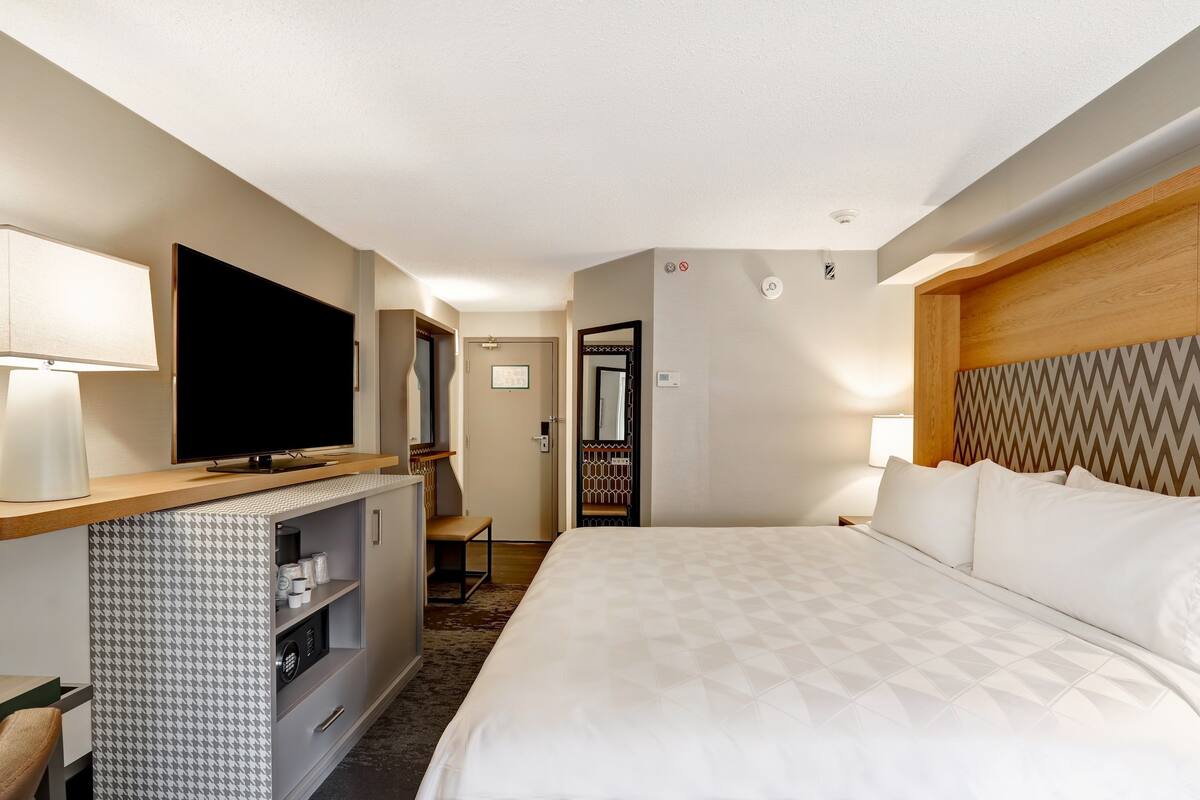 A hotel room with a large bed, a flat-screen TV, a minibar, and a desk with a chair.