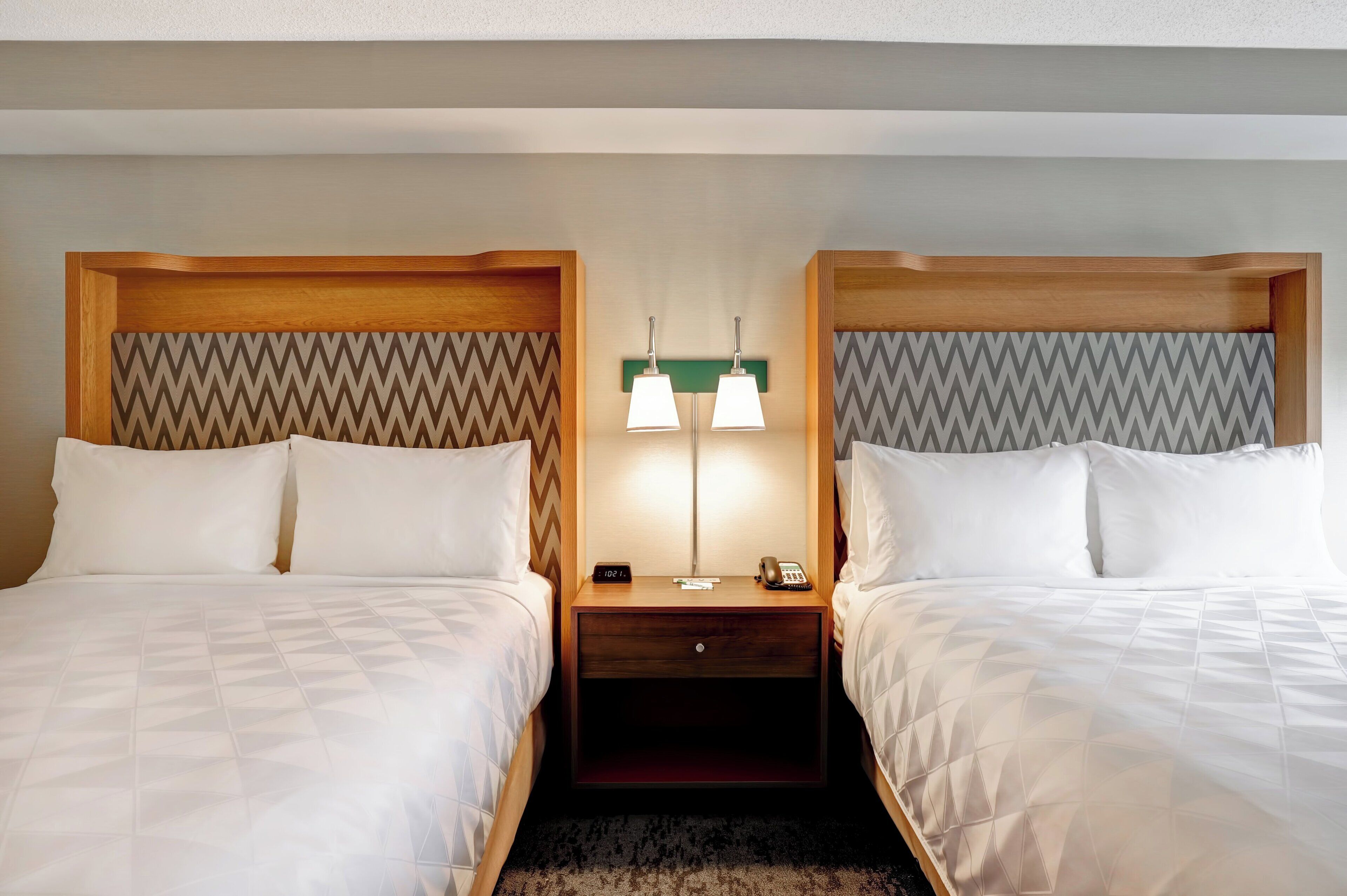 Habitación de hotel con dos camas, cabeceros de madera, una mesita de noche con lámpara y teléfono.