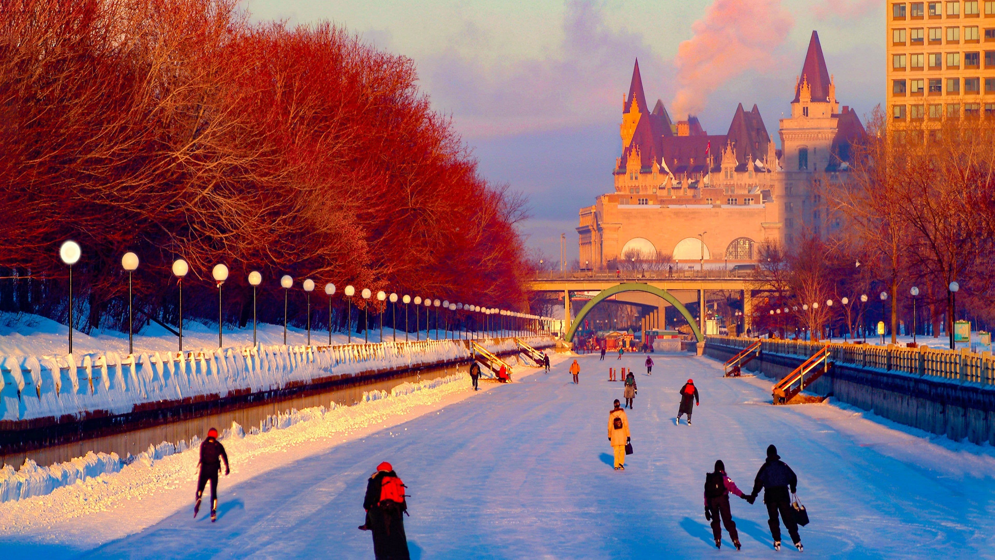 A snow-covered river with people walking, a bridge, and a historic building in the background.