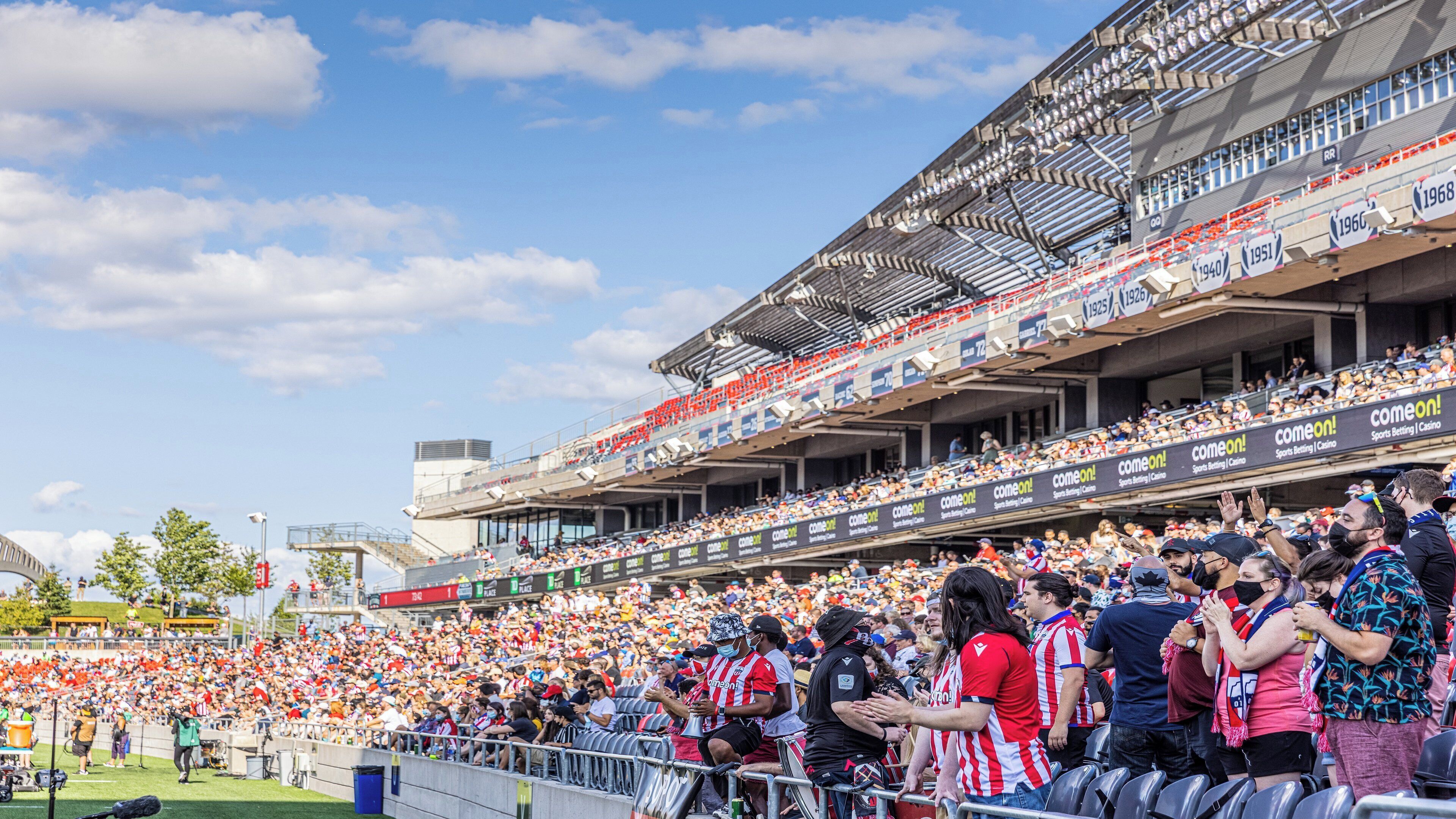 A stadium with tiered seating, advertisements, and a clear sky.