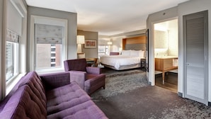 Habitación de hotel con una cama grande, un sofá, un escritorio y un baño visible a través de una puerta abierta.
