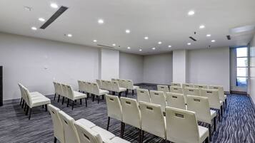 Un salón de conferencias con filas de sillas, piso alfombrado y un amplio ventanal.