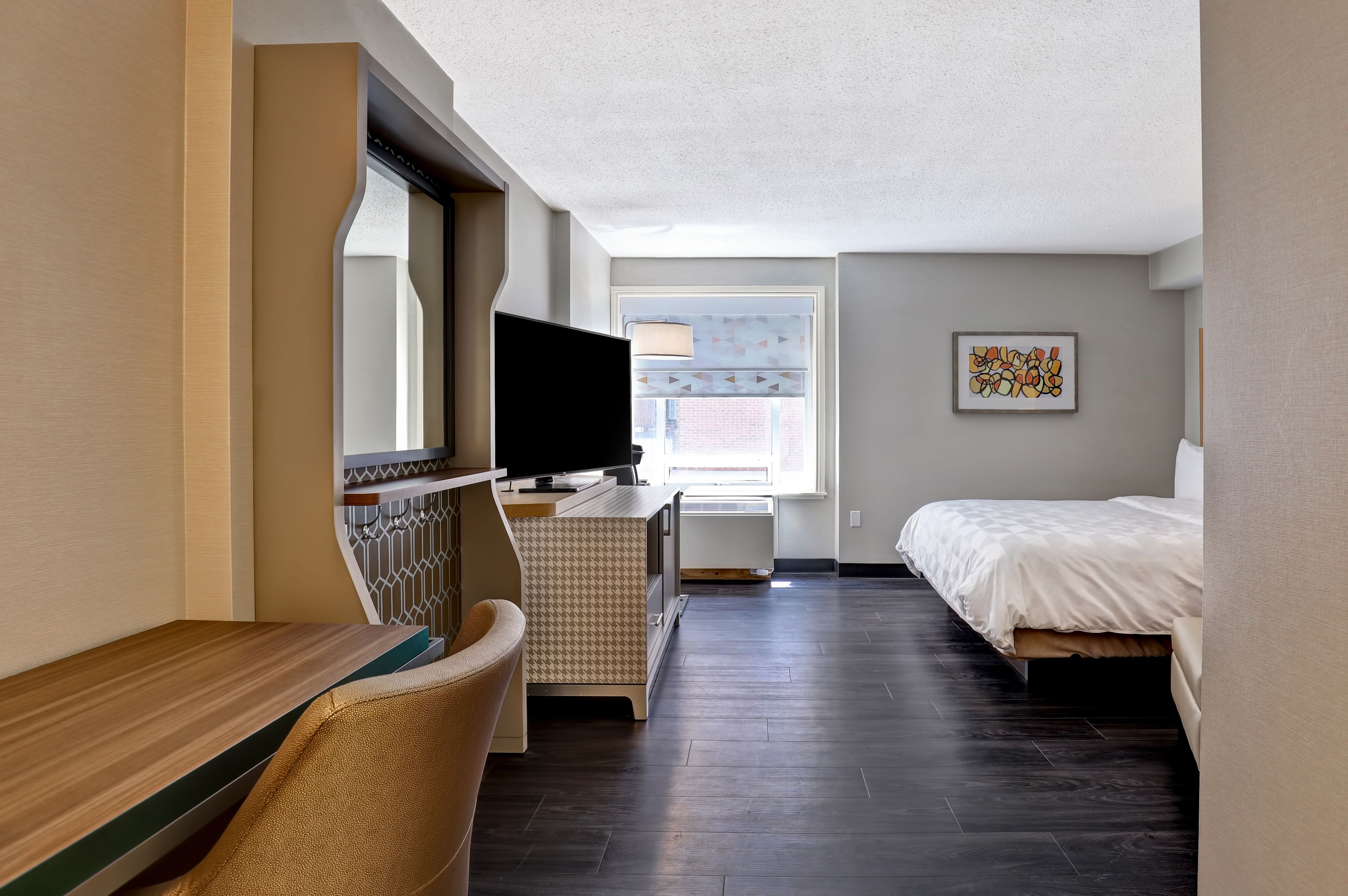 A hotel room with a bed, a desk, a chair, a television, and a window.