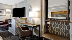 Habitación de hotel con televisor de pantalla plana, escritorio con lámpara, silla, sofá y cama con cabecero.