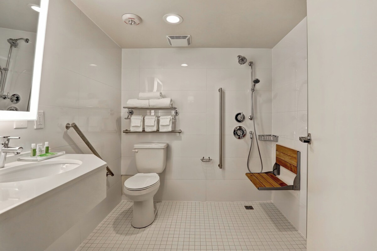 A modern bathroom with a toilet, sink, shower, and a bench.