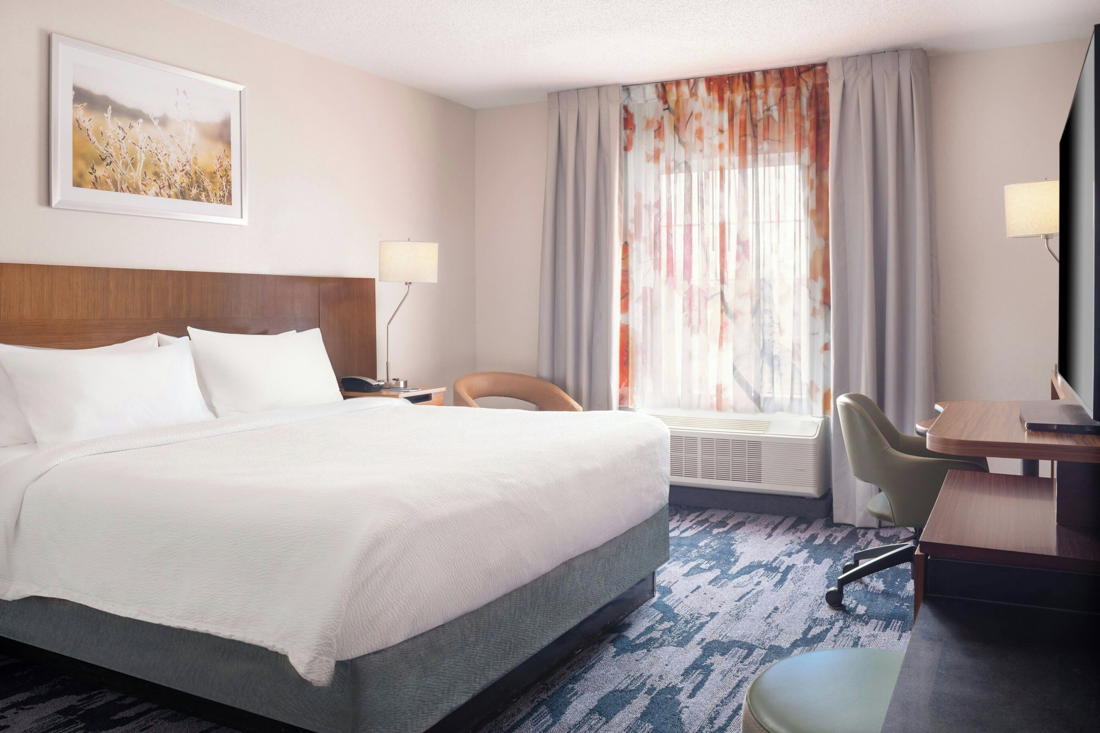 A hotel room with a large bed, a desk, a chair, a lamp, and a window with curtains.