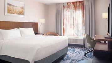 A hotel room with a large bed, a desk, a chair, a lamp, and a window with curtains.