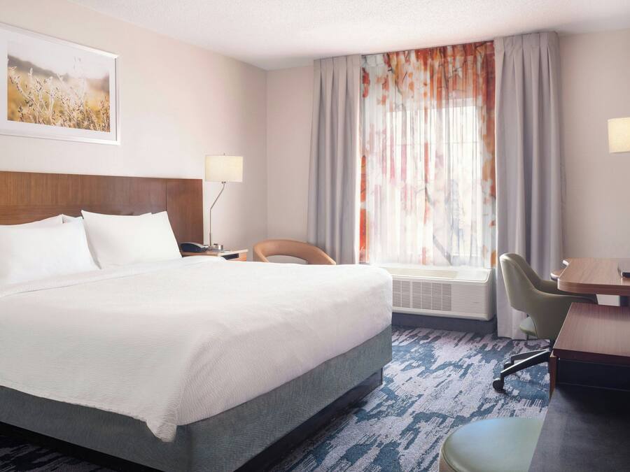 A hotel room with a large bed, a desk, a chair, a lamp, and a window with curtains.