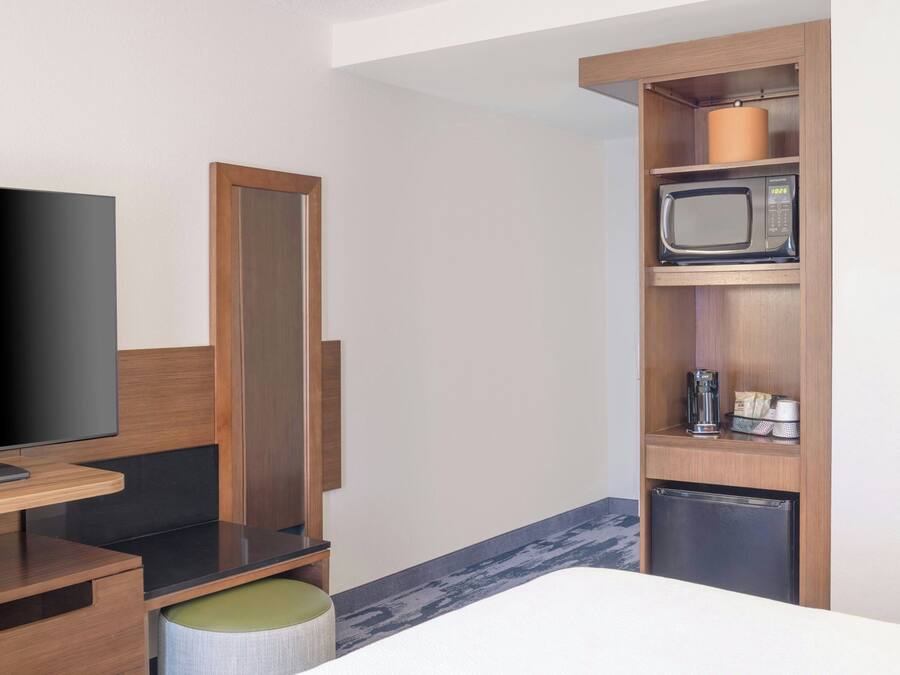 A hotel room with a television, a wooden cabinet with a microwave, and a small refrigerator.