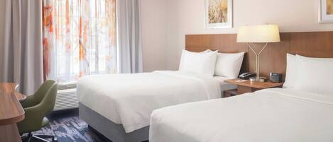 A hotel room with two beds, a desk, a chair, a lamp, and a painting on the wall.