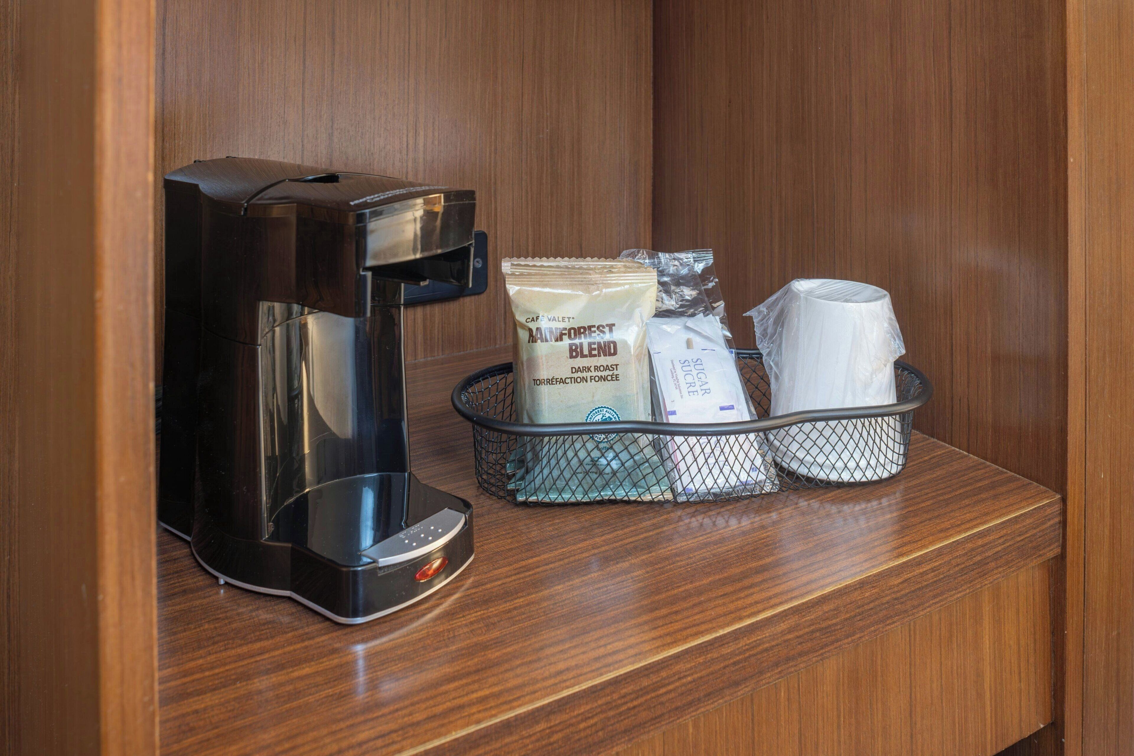 A coffee maker, a coffee pod, a cup, and a tissue box on a wooden counter.