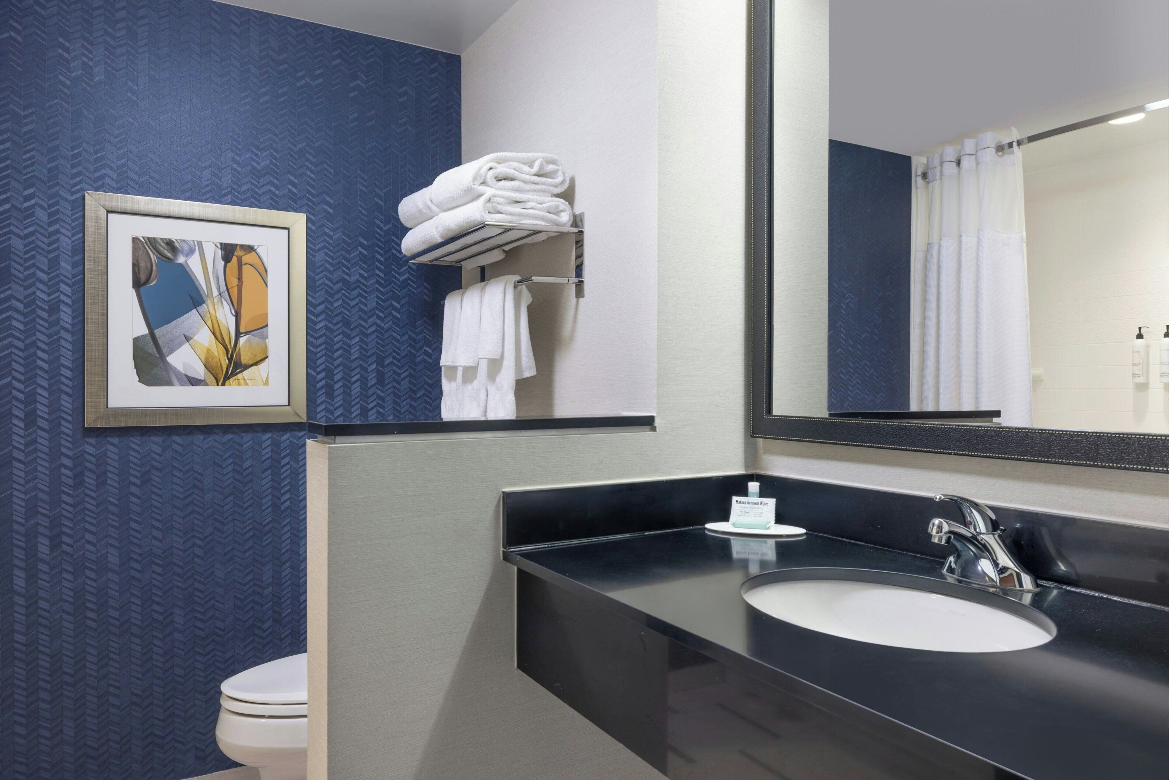 Une salle de bain avec des toilettes blanches, un lavabo noir, un miroir et un porte-serviettes avec des serviettes pliées.