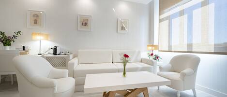 A modern living room with a white sofa, two armchairs, a wooden coffee table, and a large window with a view.