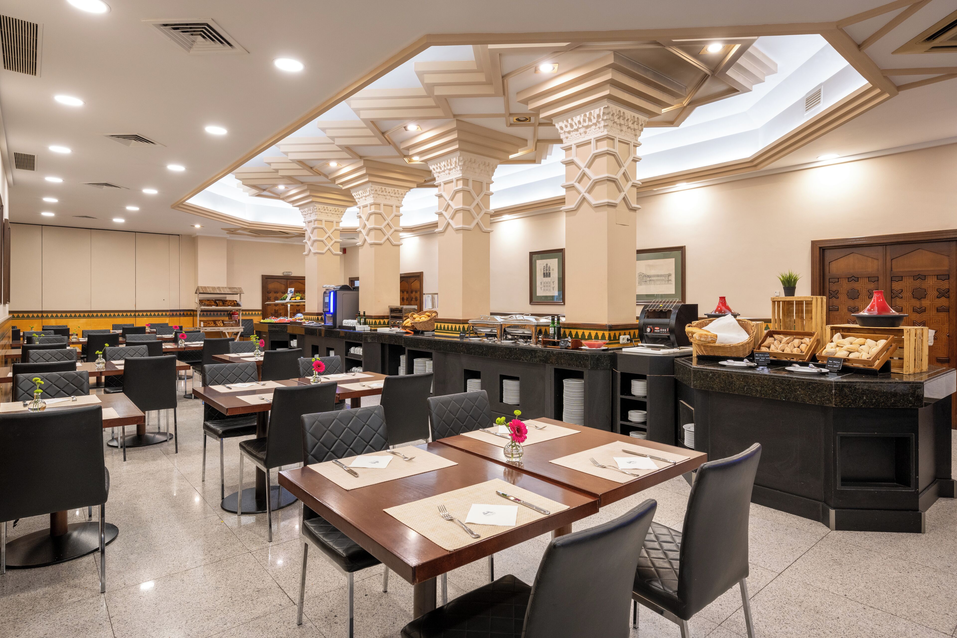 Un restaurante amplio con varias mesas y sillas, una barra con exhibición de alimentos y un diseño de techo moderno.