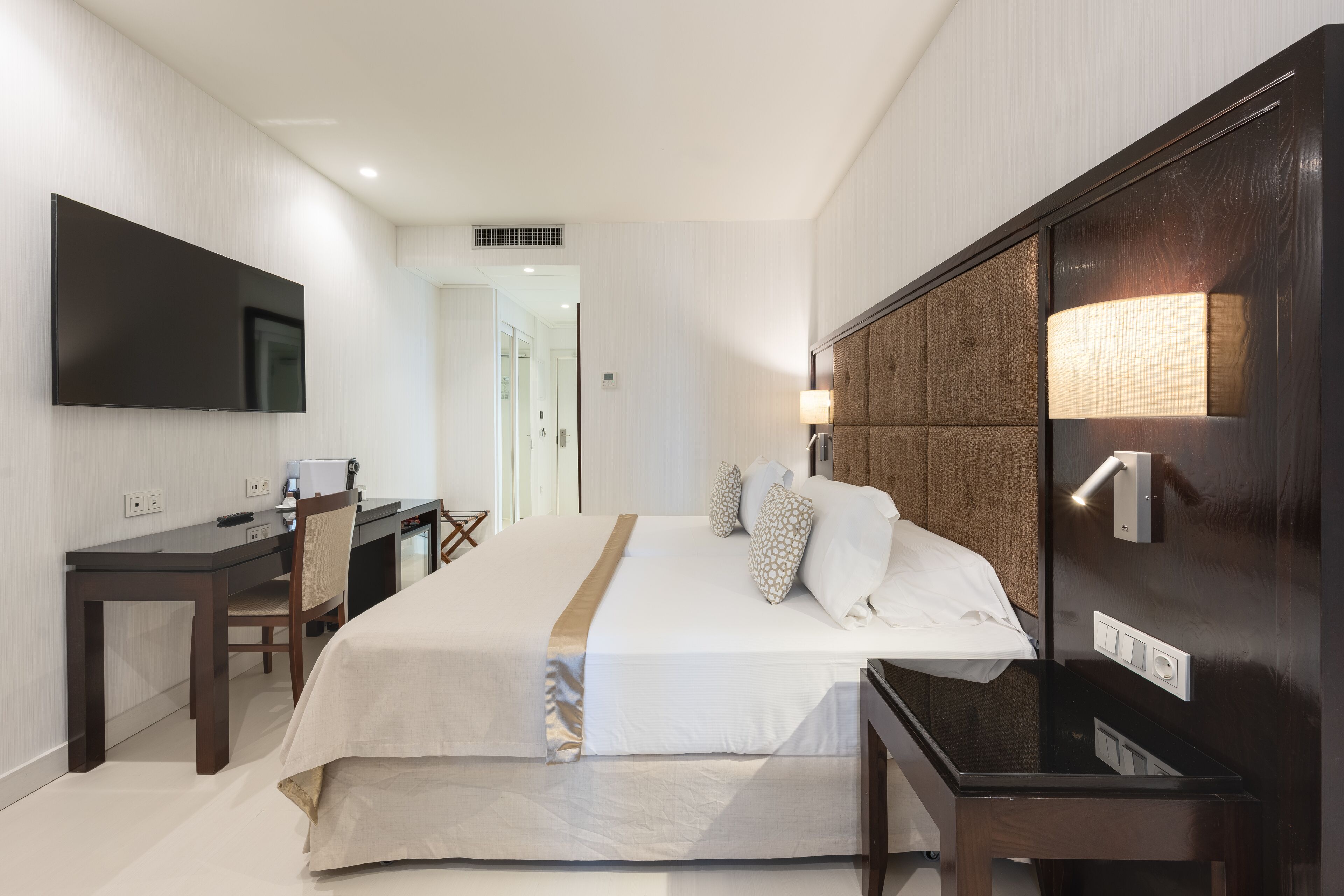 Una habitación de hotel con una cama grande, un escritorio, un televisor de pantalla plana y una mesita de noche con lámpara.