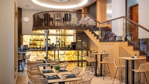 A modern restaurant with wicker furniture, a bar area, and a staircase leading to an upper level.