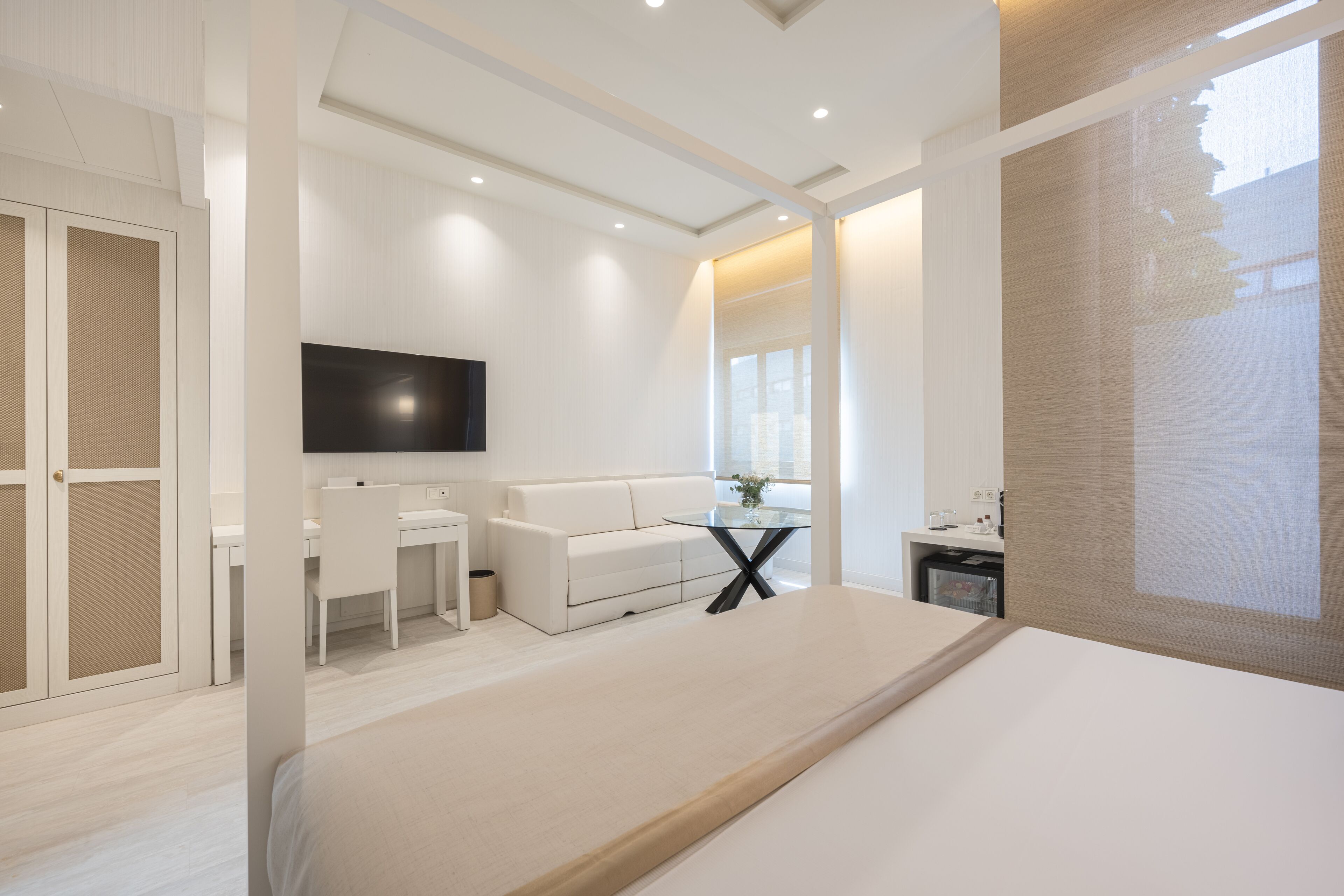 A modern hotel room with a bed, a desk, a sofa, and a TV.