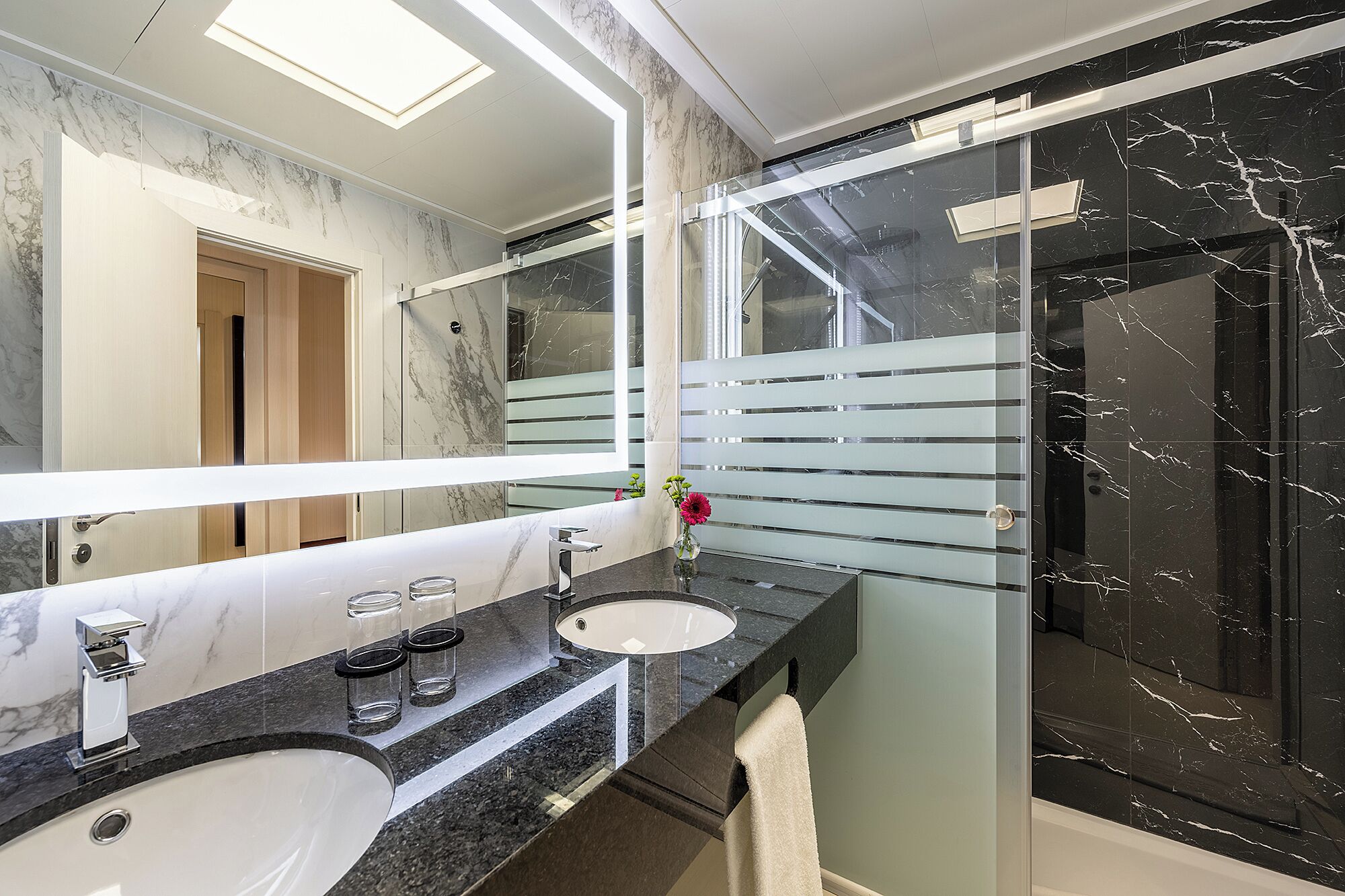 A modern bathroom with a marble vanity, a glass shower enclosure, and a large mirror.