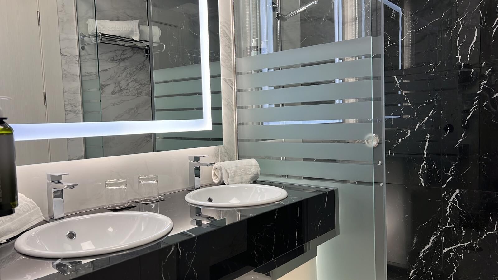 A modern bathroom with two sinks, a large mirror, and marble walls.
