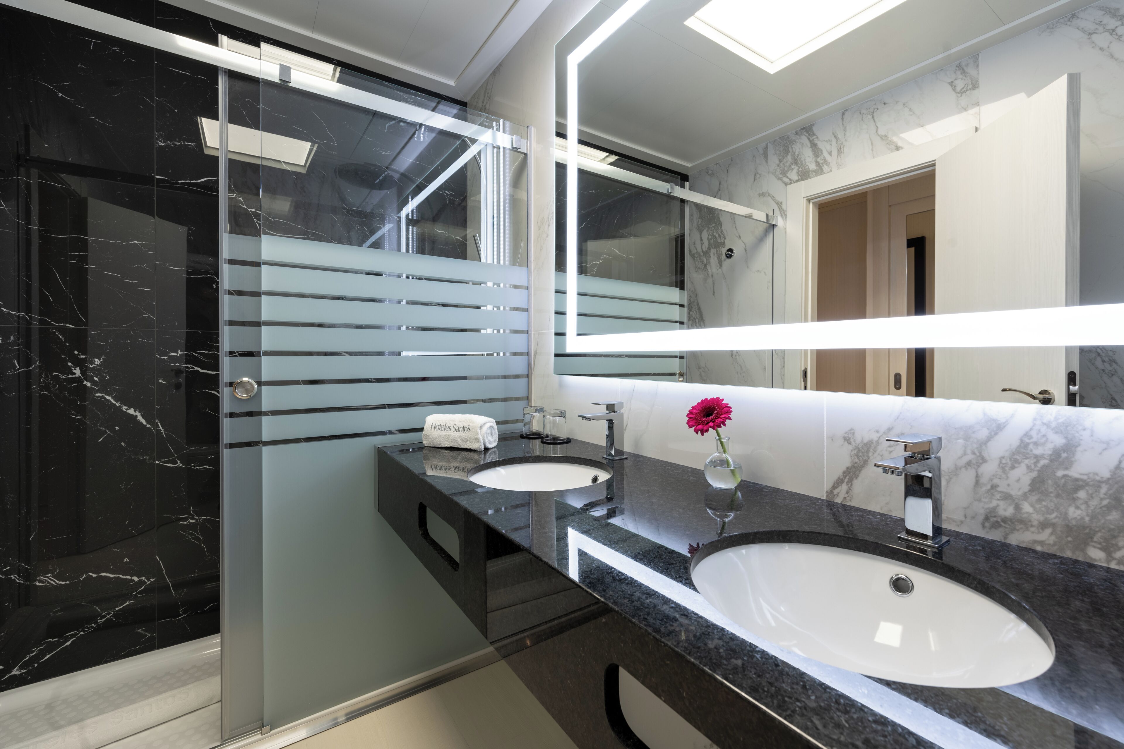 A modern bathroom with a glass shower enclosure, two sinks, and a large mirror.