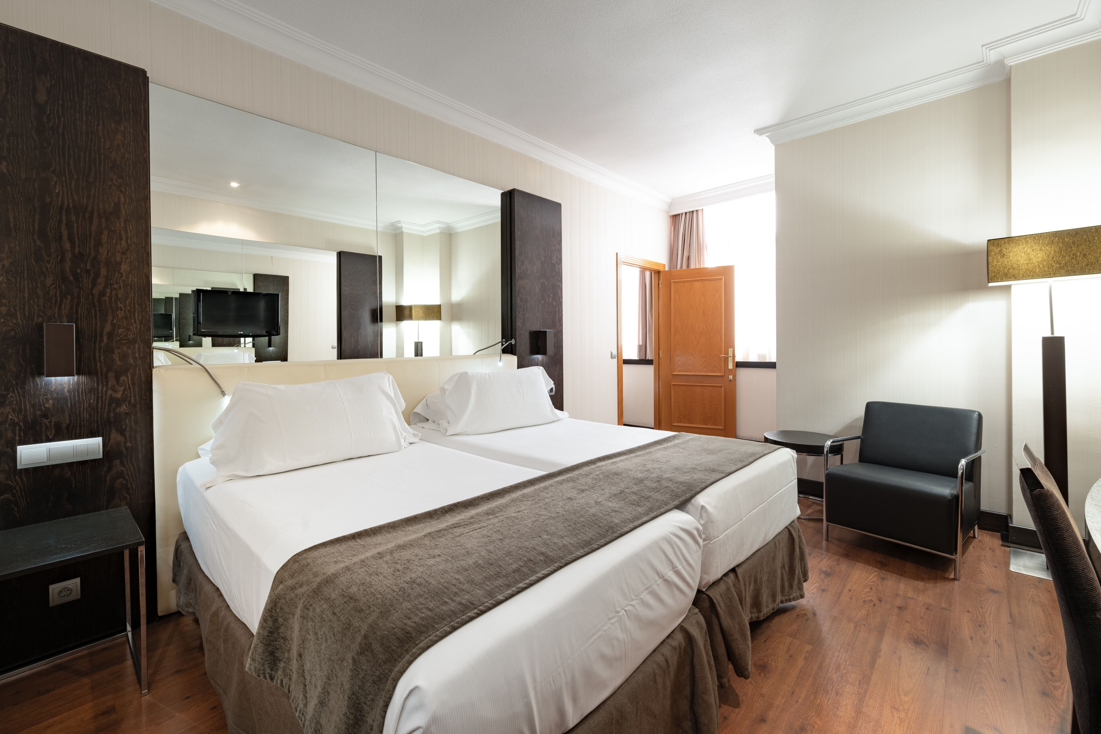 Een hotelkamer met een groot bed, een stoel, een bureau, een televisie en een spiegel.