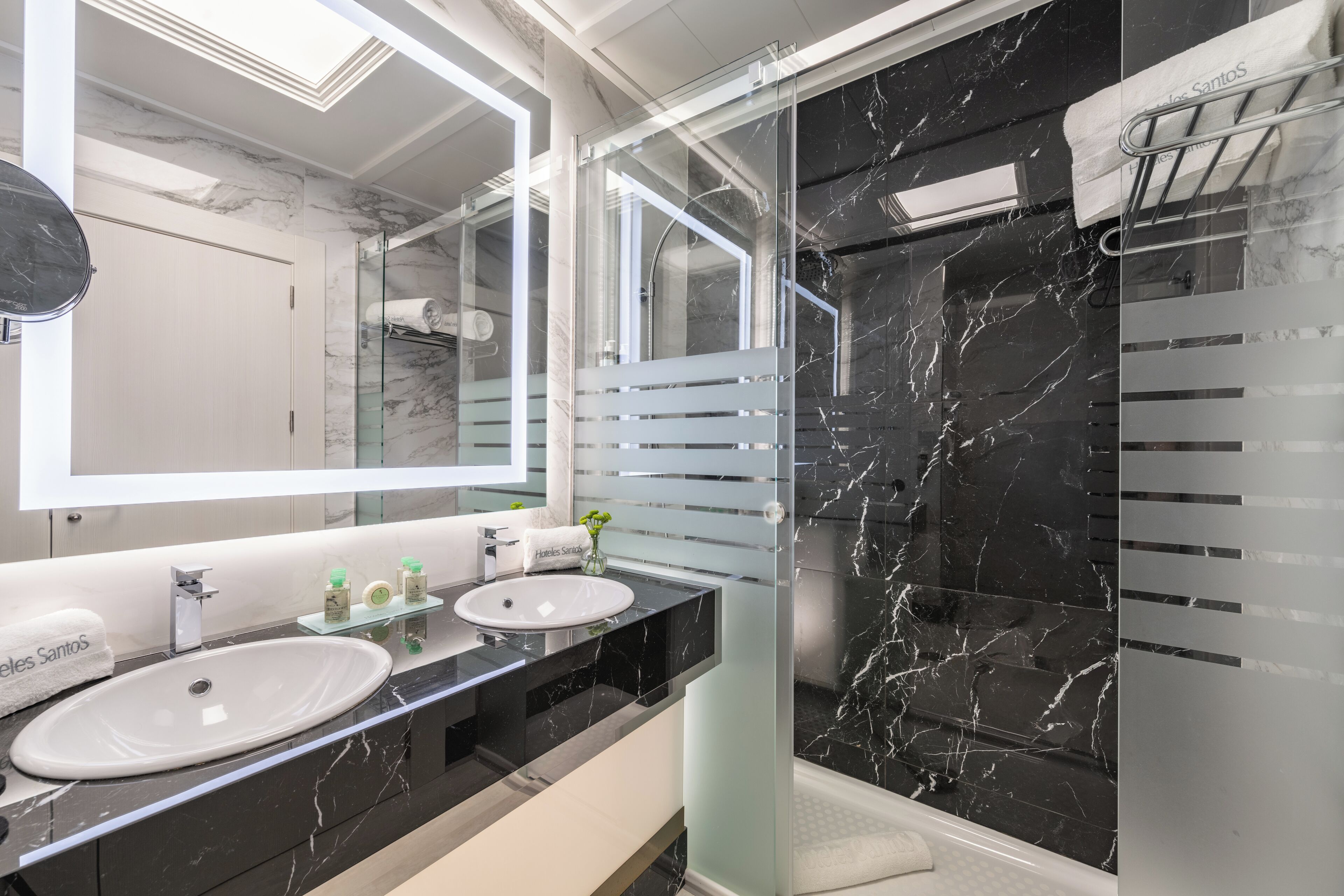 Un baño moderno con dos lavamanos, un espejo grande y ducha con mampara de vidrio.