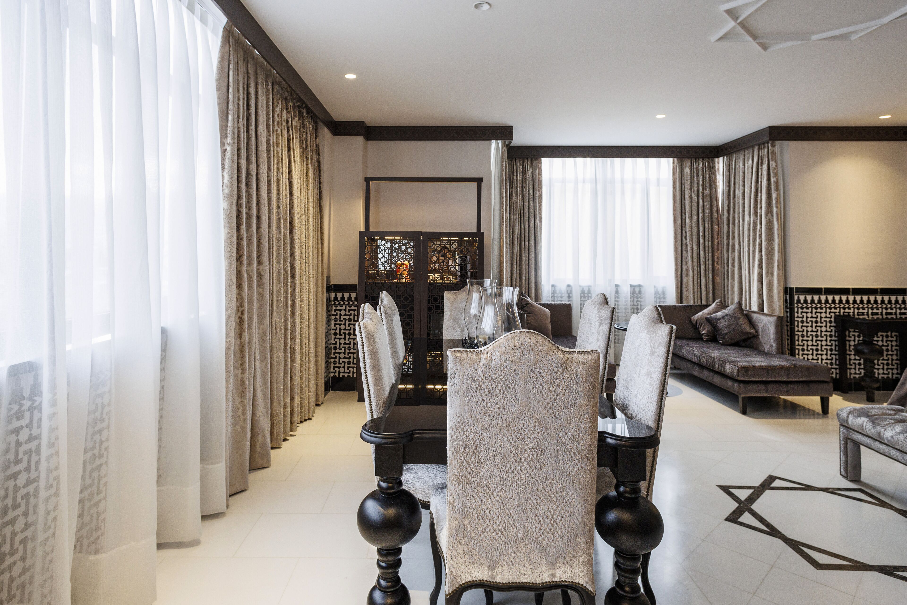 A modern living room with a dining area, featuring a sofa, chairs, and a decorative screen.