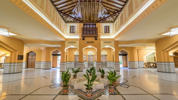 A spacious lobby with a high ceiling, ornate ceiling design, and a central seating area with potted plants.