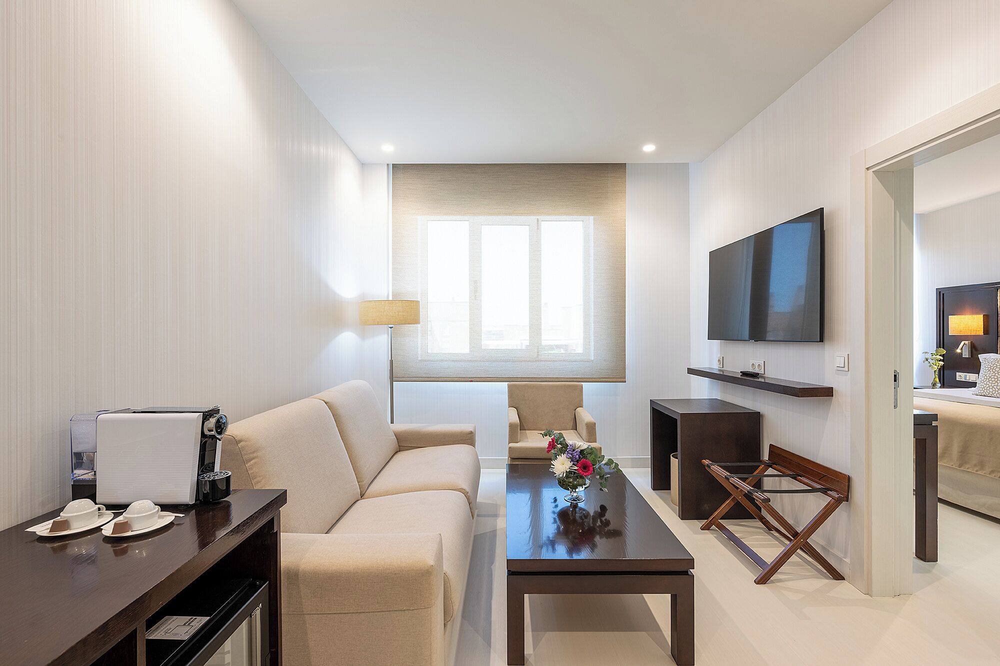 A modern living room with a sofa, coffee table, TV, and a small dining area with a table and chairs.