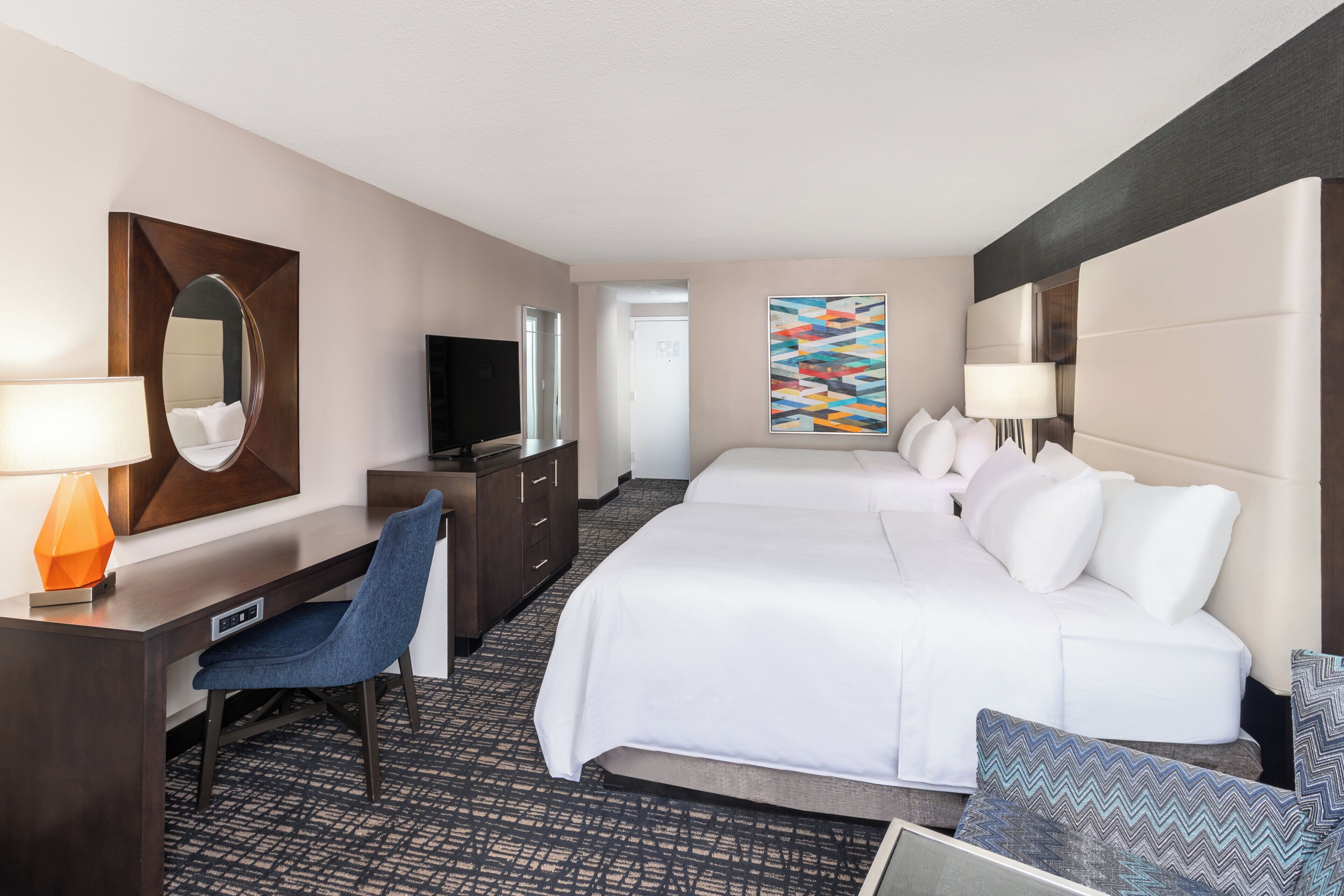 A hotel room with a large bed, a desk with a chair, a television, and a painting on the wall.