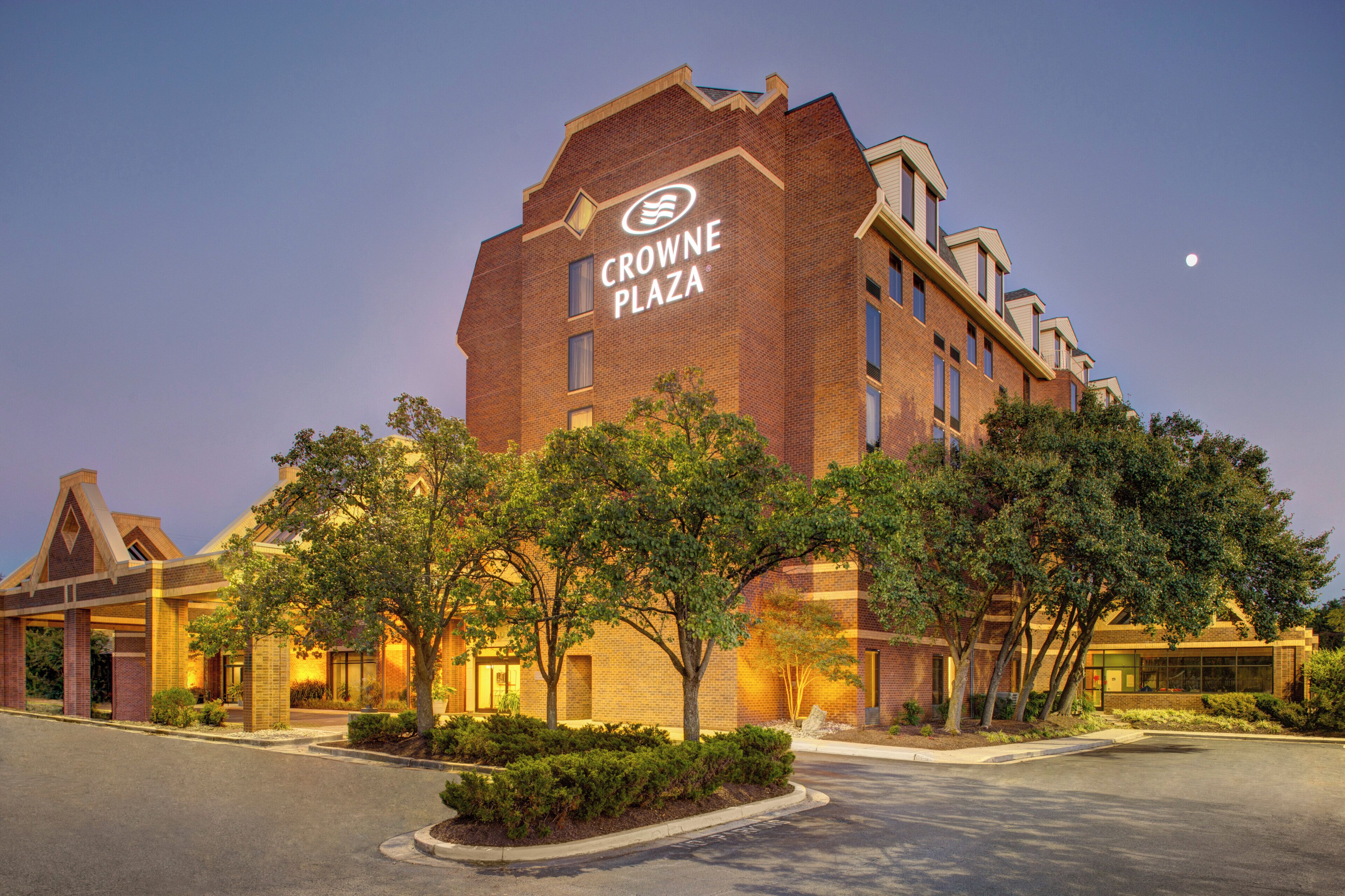 A hotel with a prominent sign reading 'Crowne Plaza' on the facade, surrounded by trees and a well-maintained lawn.