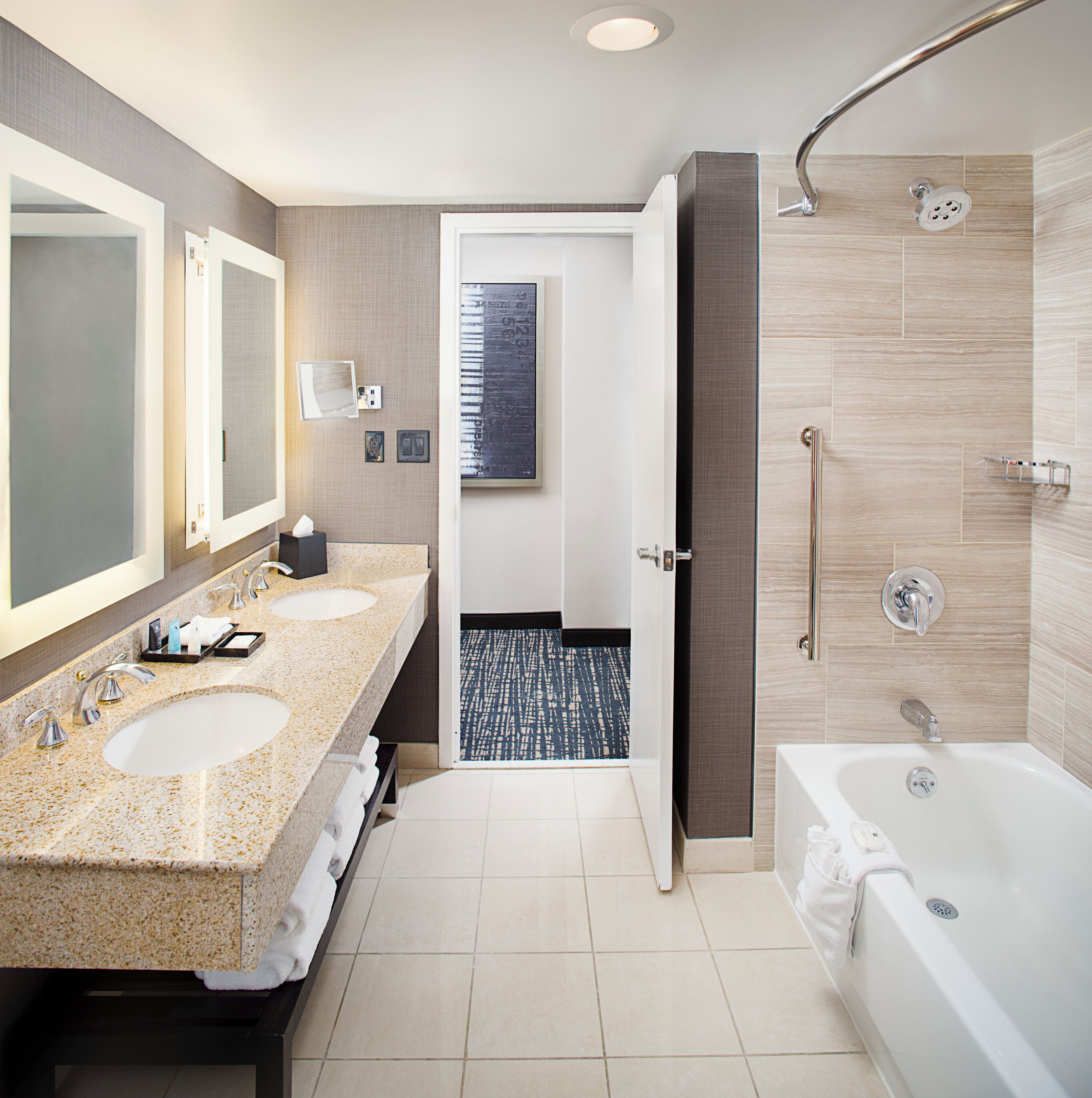 A modern bathroom with dual sinks, a large mirror, a shower with a curved glass door, and a tiled floor.
