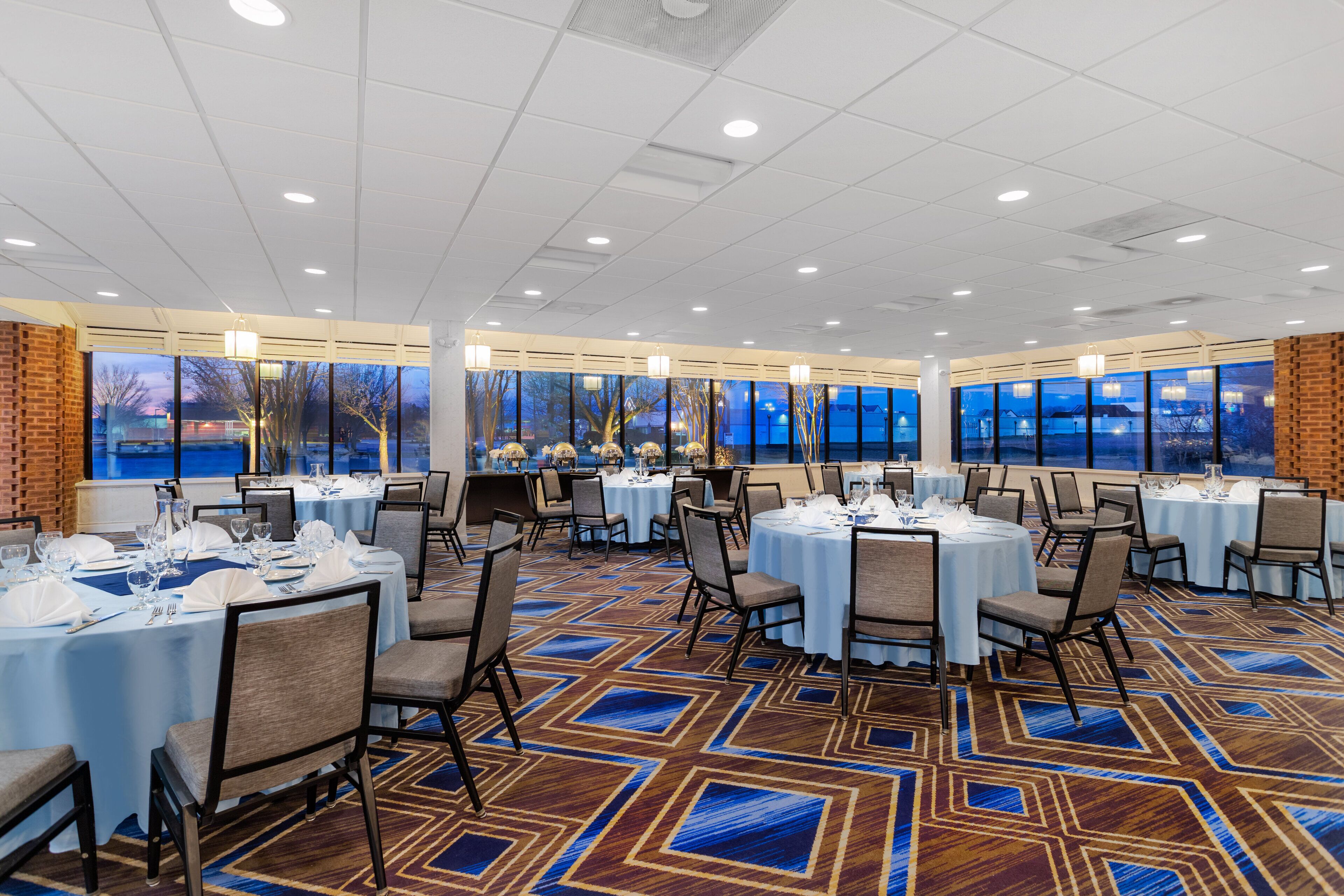 A banquet hall with round tables, chairs, and a patterned carpet.