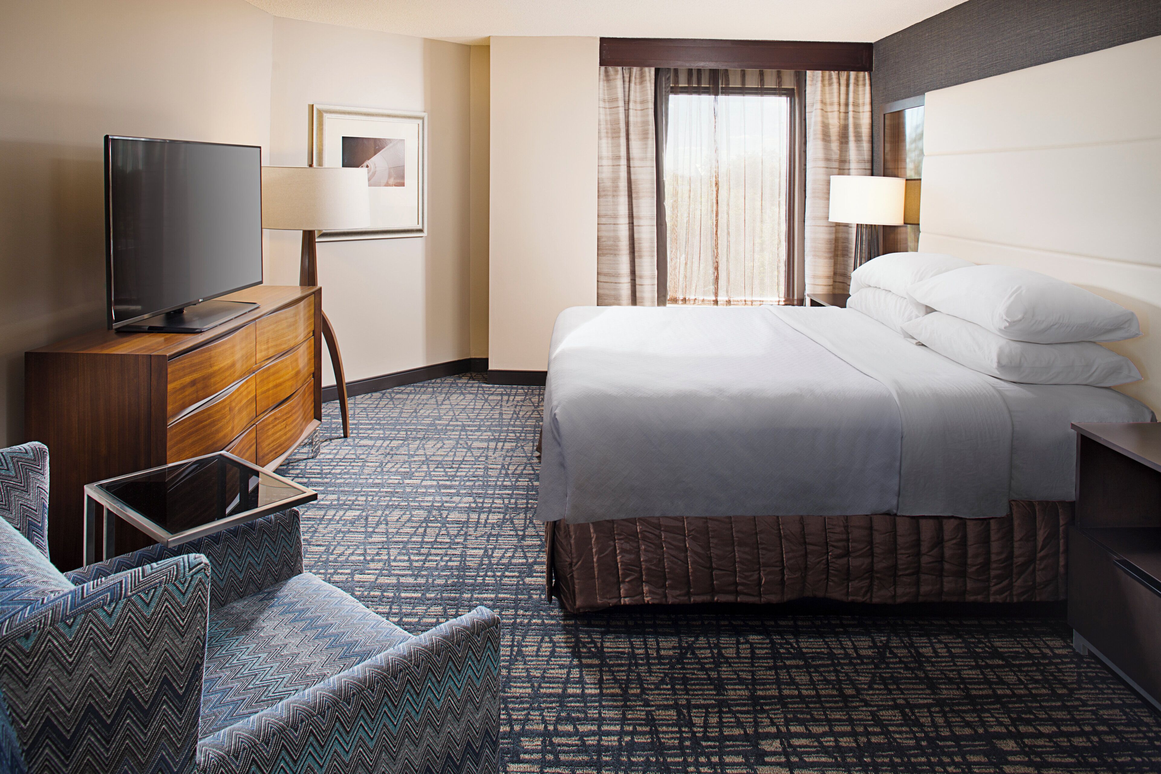 A hotel room with a bed, a TV, a desk, and a chair.