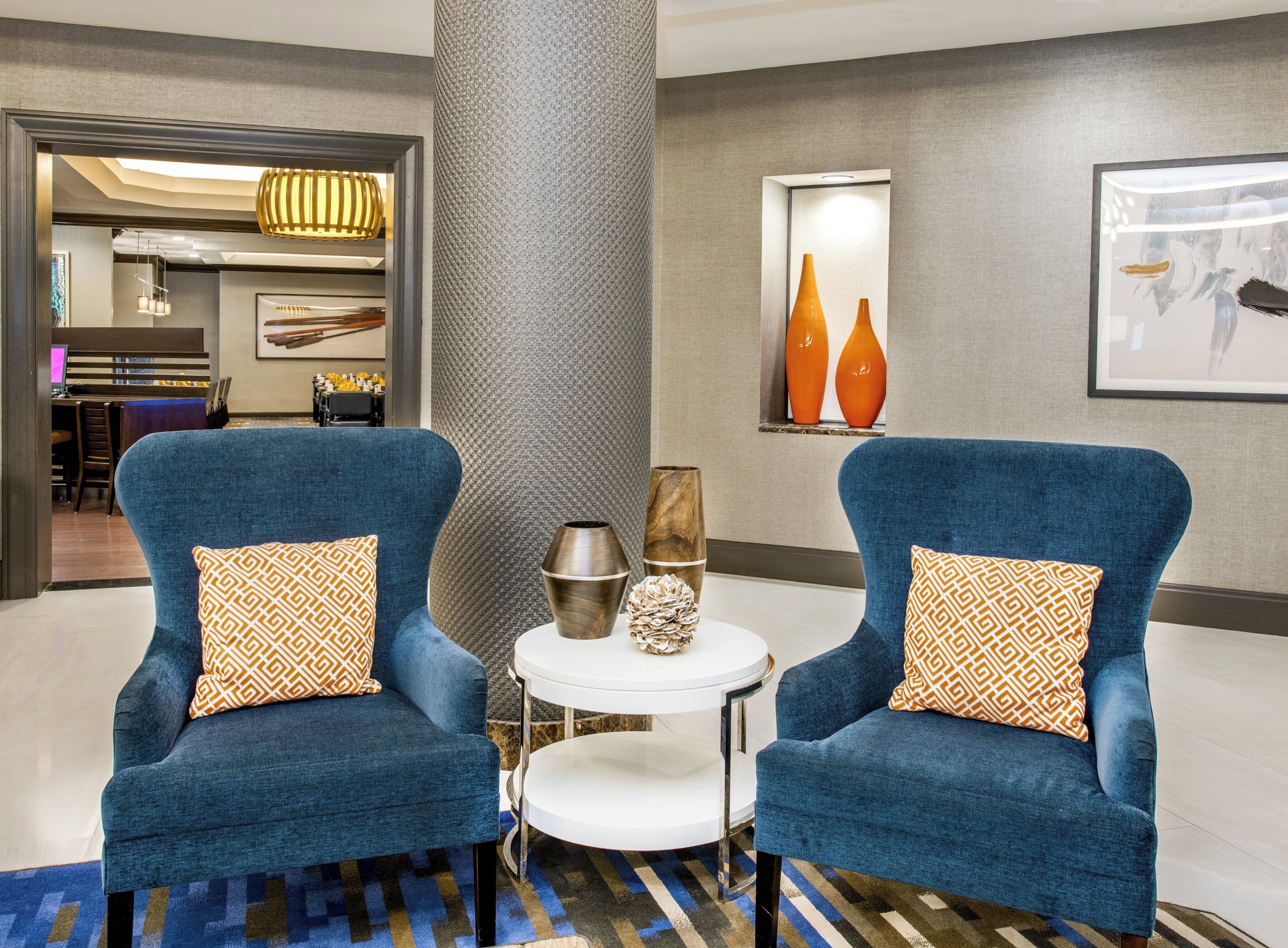 Eine moderne Lobby mit zwei blauen Sesseln, einem runden Tisch und einer großen Säule.
