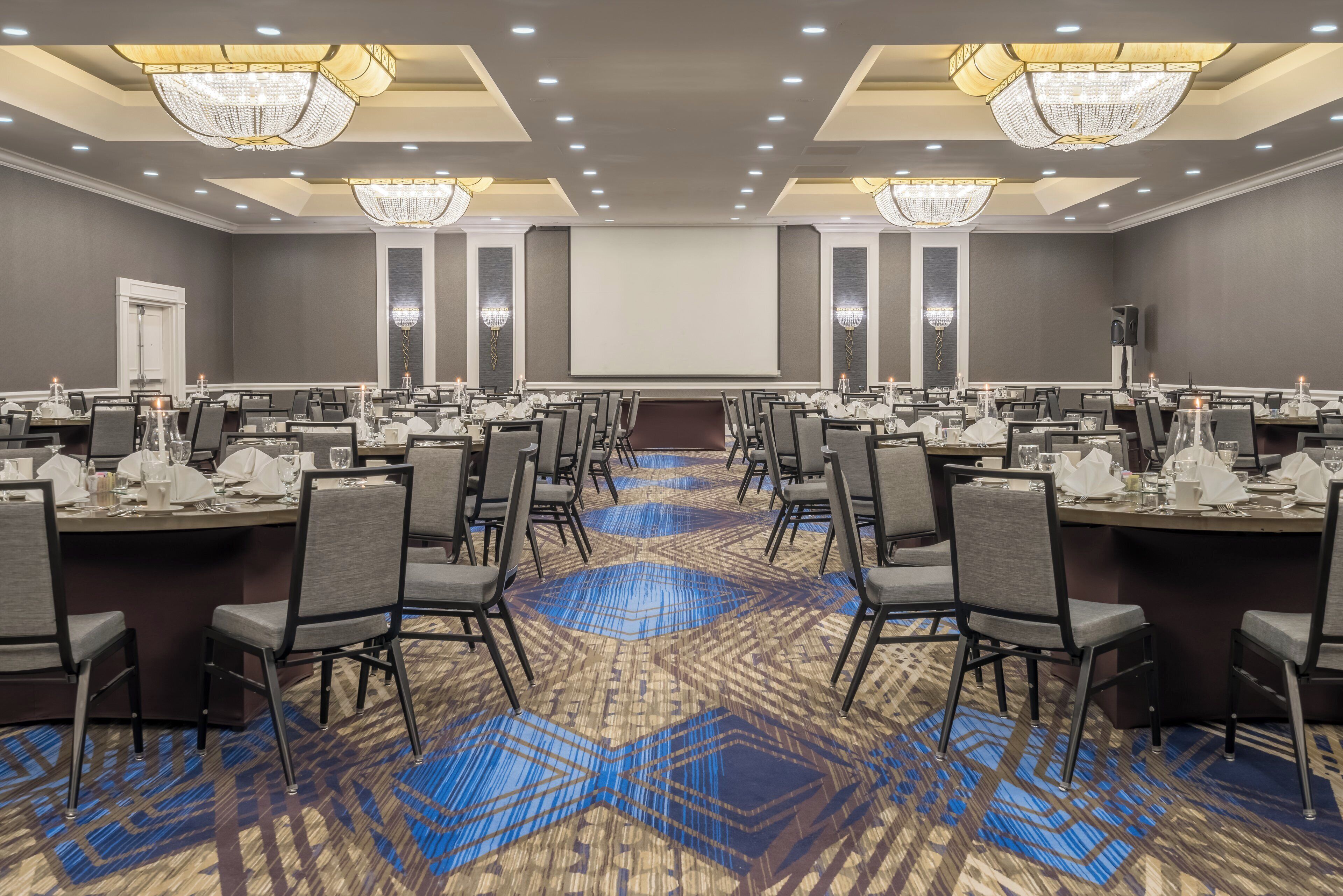 A conference room with multiple tables, chairs, and a large screen at the front.