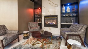 Uma sala de estar moderna com dois poltronas cinzas, uma mesa de centro redonda, uma lareira e estantes decorativas.